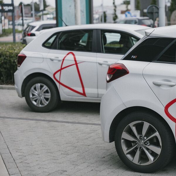 Two white cars with the red Axintor Interim logo on the sides, parked next to each other in a parking lot.