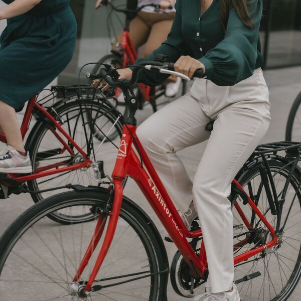 Mensen fietsen op rode Axintor Interim fietsen, met focus op de fiets en benen van de voorste persoon.